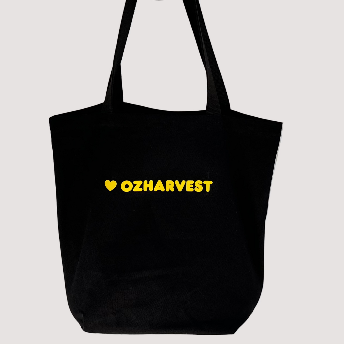 Black tote bag with 'OZHAVEST' text on a light gray textured wall v 1