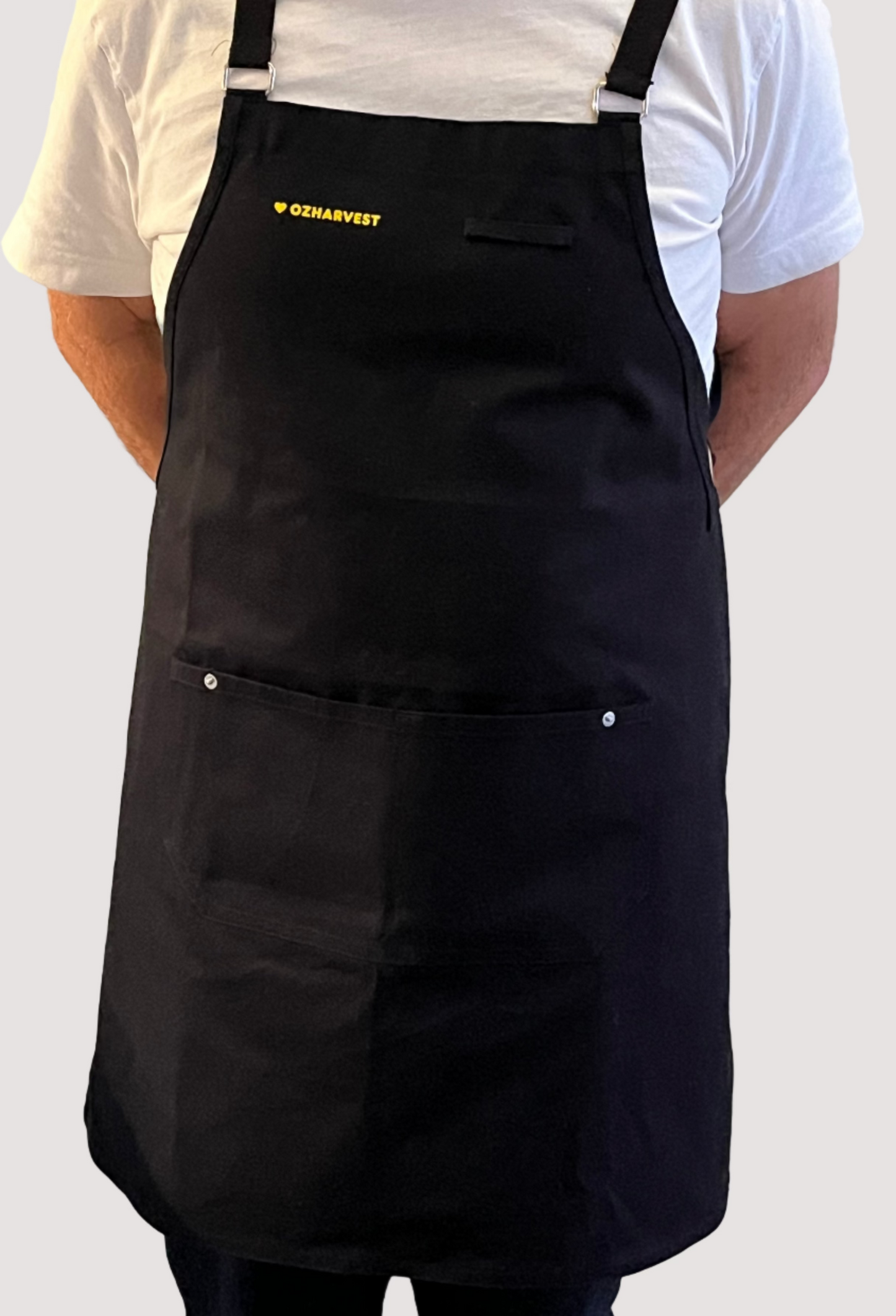 Wearing a black apron with a brand logo against a white brick wall.