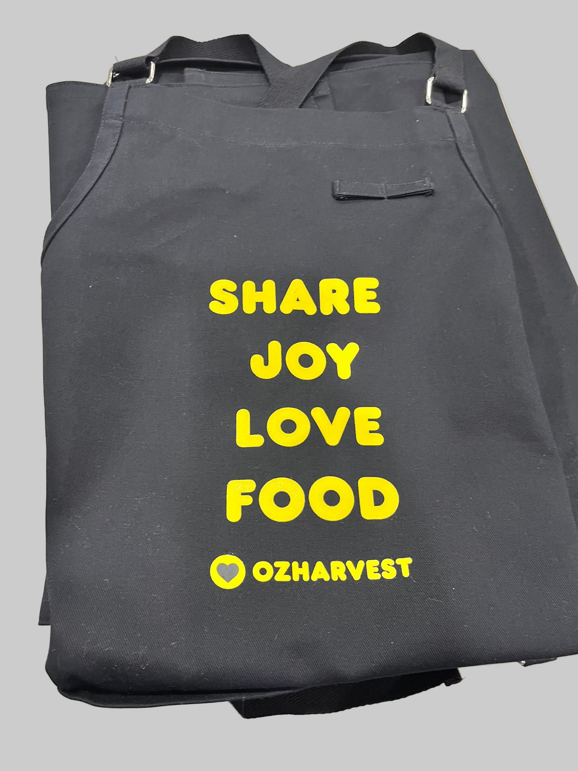 Black apron with yellow text 'SHARE JOY LOVE FOOD' and 'OZHAVESRT' logo on a white background