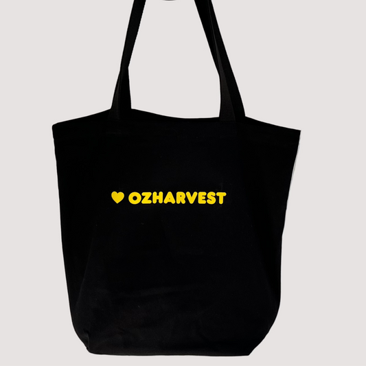 Black tote bag with 'OZHAVEST' text on a light gray textured wall v 1