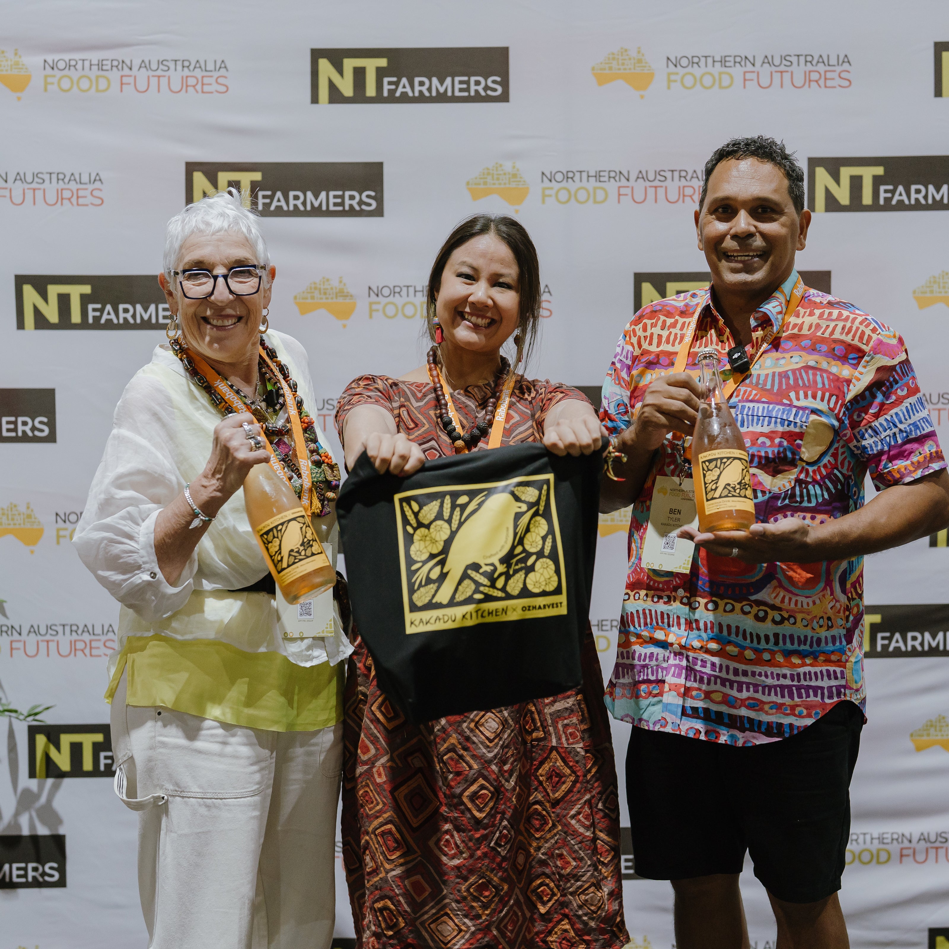 Three people holding bottles and a framed item in front of an NT Farmers backdrop