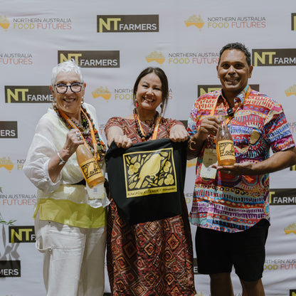 Three people holding bottles and a framed item in front of an NT Farmers backdrop