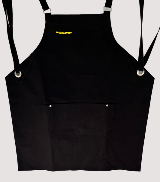 Black apron with a brand logo hanging against a white brick wall.